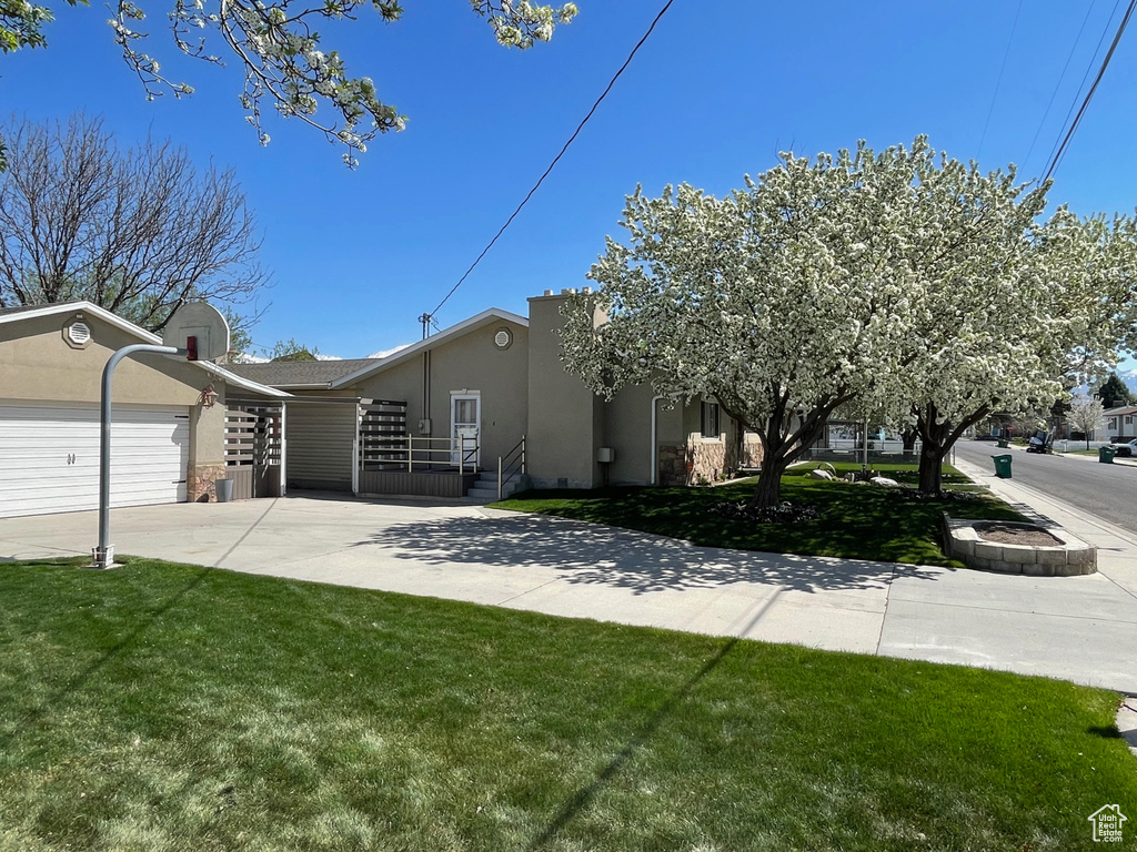 View of front of property with stucco siding, concrete driveway, a front lawn, and a garage