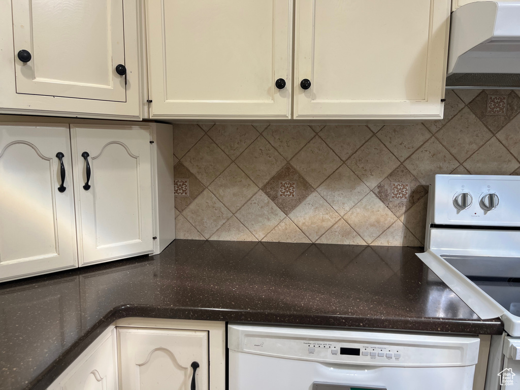 Kitchen with white appliances, wall chimney range hood, decorative backsplash, and white cabinets