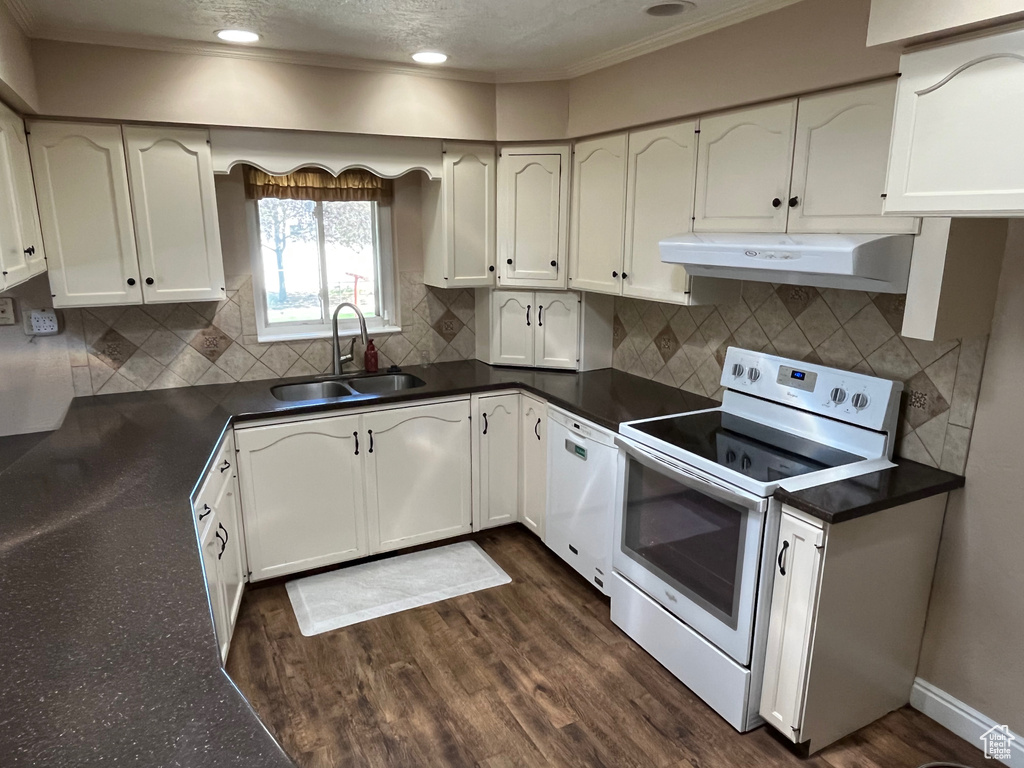Kitchen featuring white appliances, under cabinet range hood, a sink, dark countertops, and crown molding