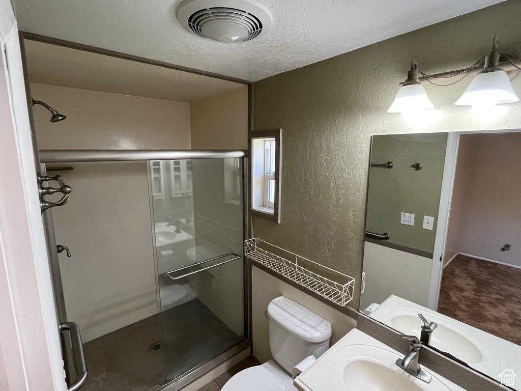 Bathroom featuring a textured wall, a shower stall, toilet, vanity, and a textured ceiling