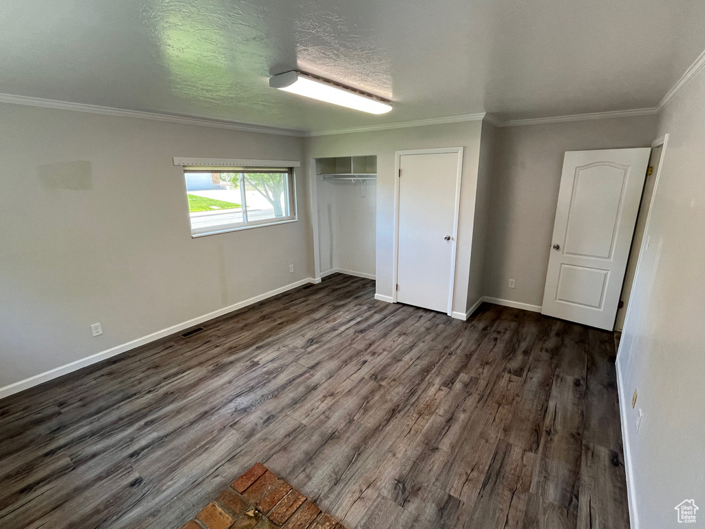 Unfurnished bedroom with dark wood-style flooring, baseboards, crown molding, and a closet