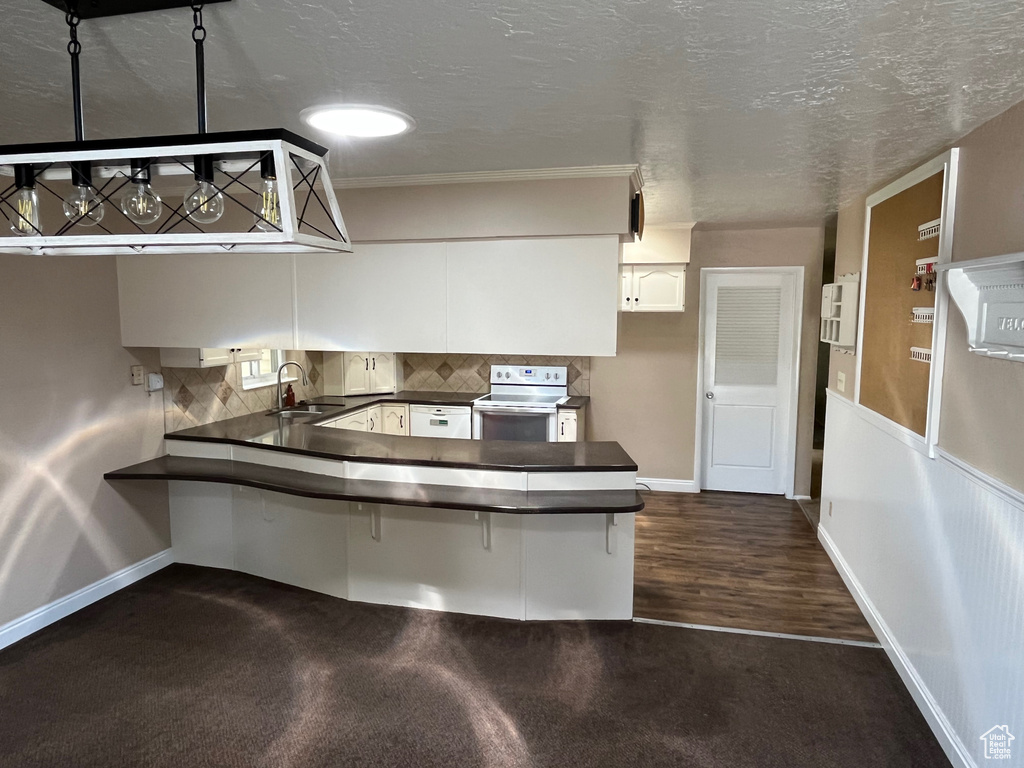 Kitchen featuring white electric range oven, a sink, dark countertops, a peninsula, and baseboards