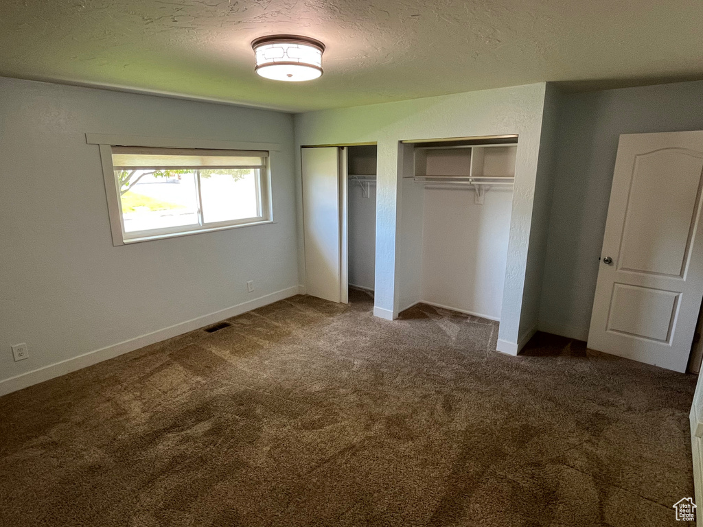 Unfurnished bedroom featuring two closets, carpet, baseboards, and a textured ceiling