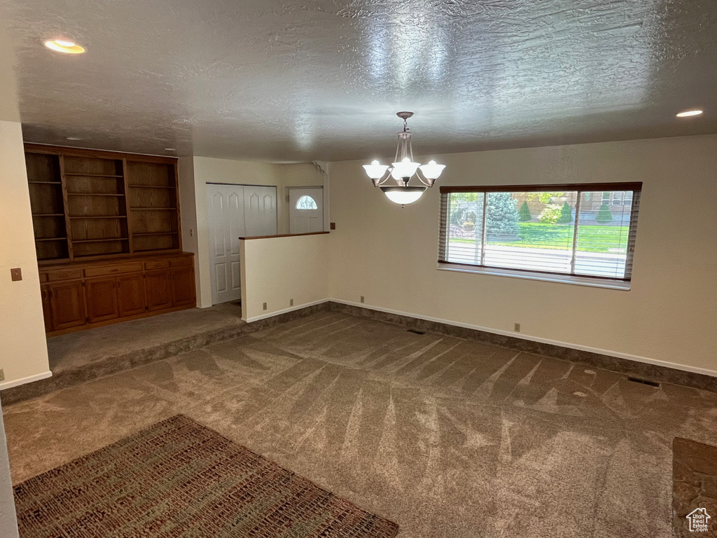 Unfurnished room featuring a chandelier, healthy amount of natural light, dark colored carpet, a textured ceiling, and recessed lighting