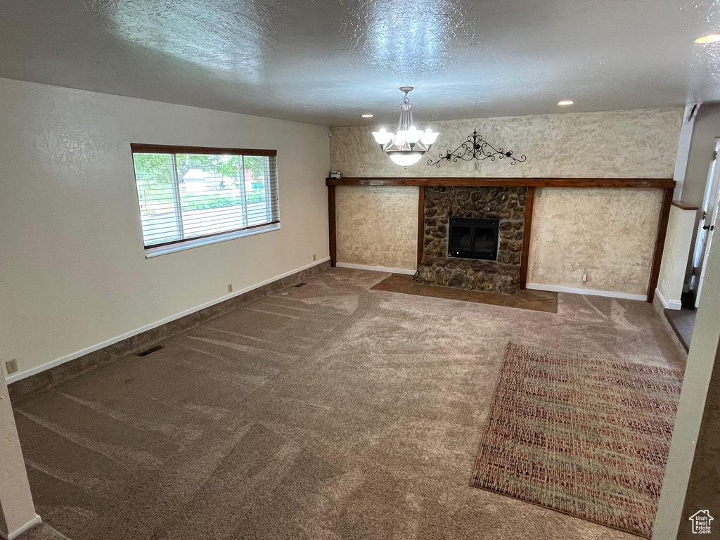 Unfurnished living room with a chandelier, a textured ceiling, carpet flooring, baseboards, and a fireplace