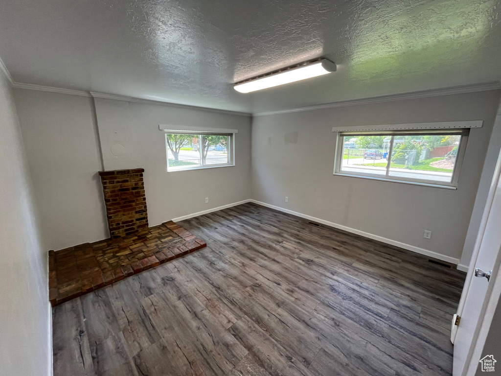 Spare room with healthy amount of natural light, dark wood-style flooring, ornamental molding, a textured ceiling, and baseboards