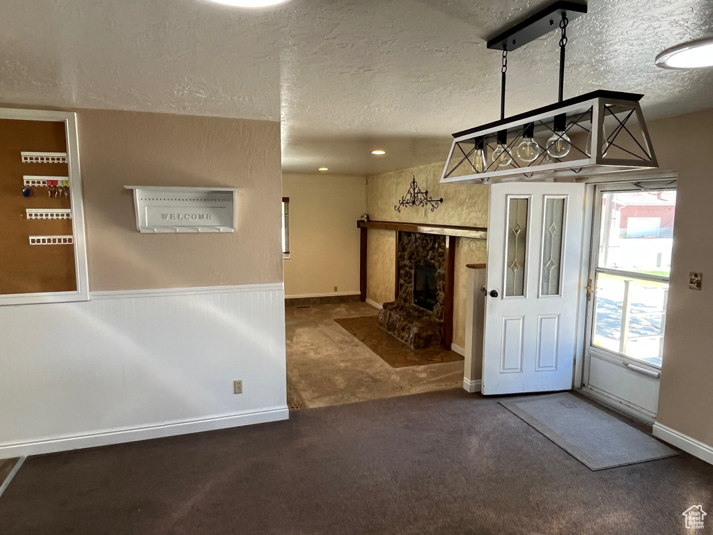 Carpeted entryway with a textured ceiling, a high end fireplace, and wainscoting