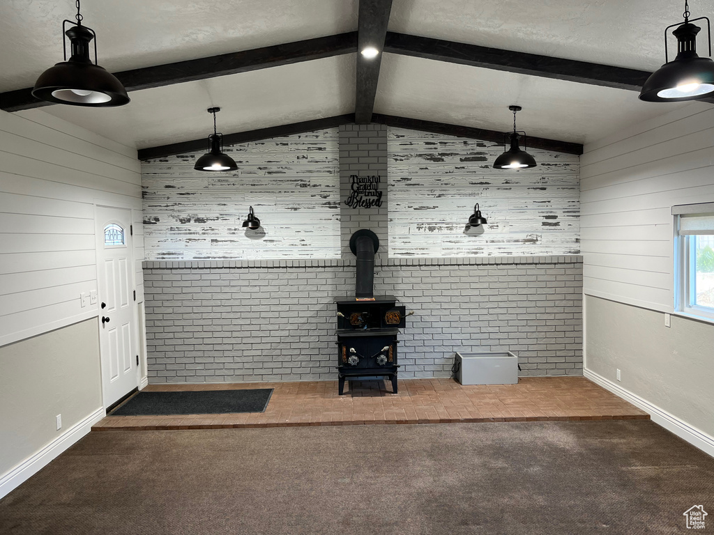 Unfurnished living room with wooden walls, carpet floors, a wood stove, baseboards, and brick wall
