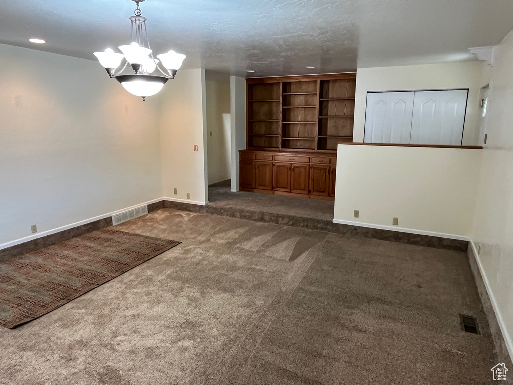 Empty room with dark carpet, a chandelier, and baseboards