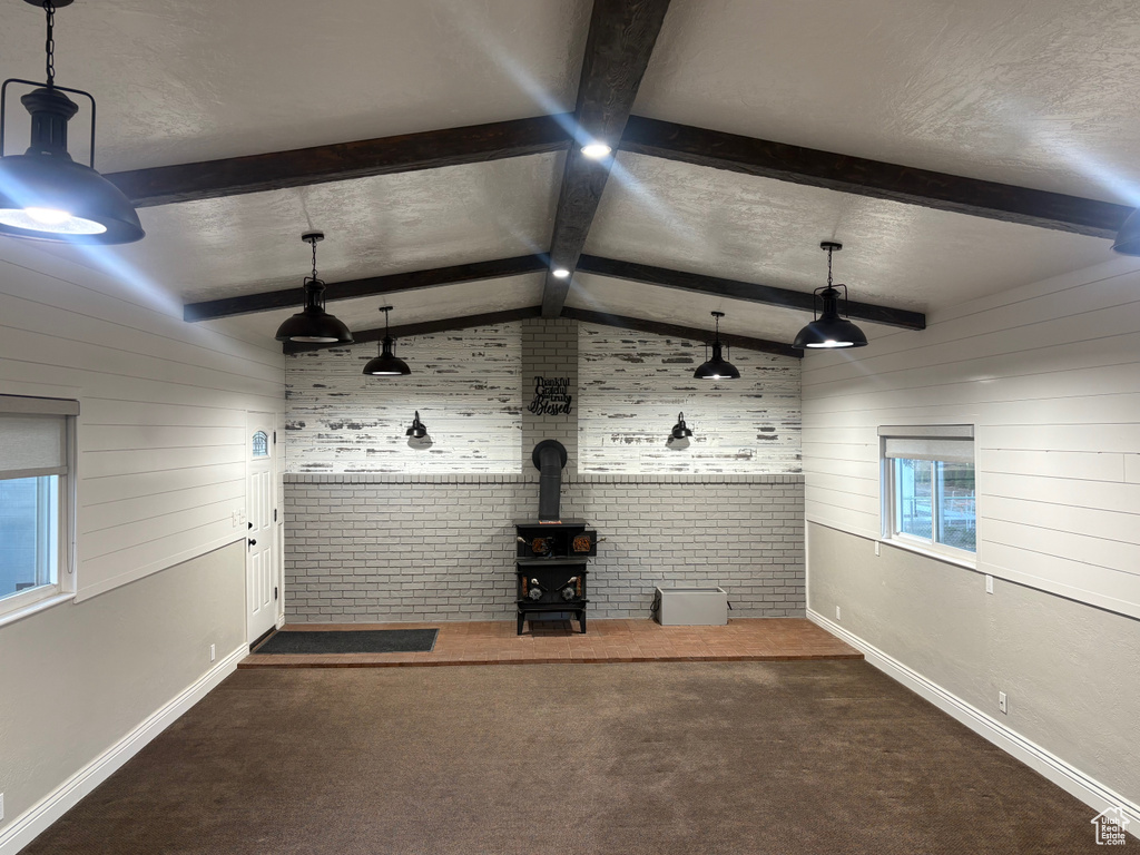 Unfurnished living room with a wood stove, baseboards, wood walls, carpet flooring, and brick wall