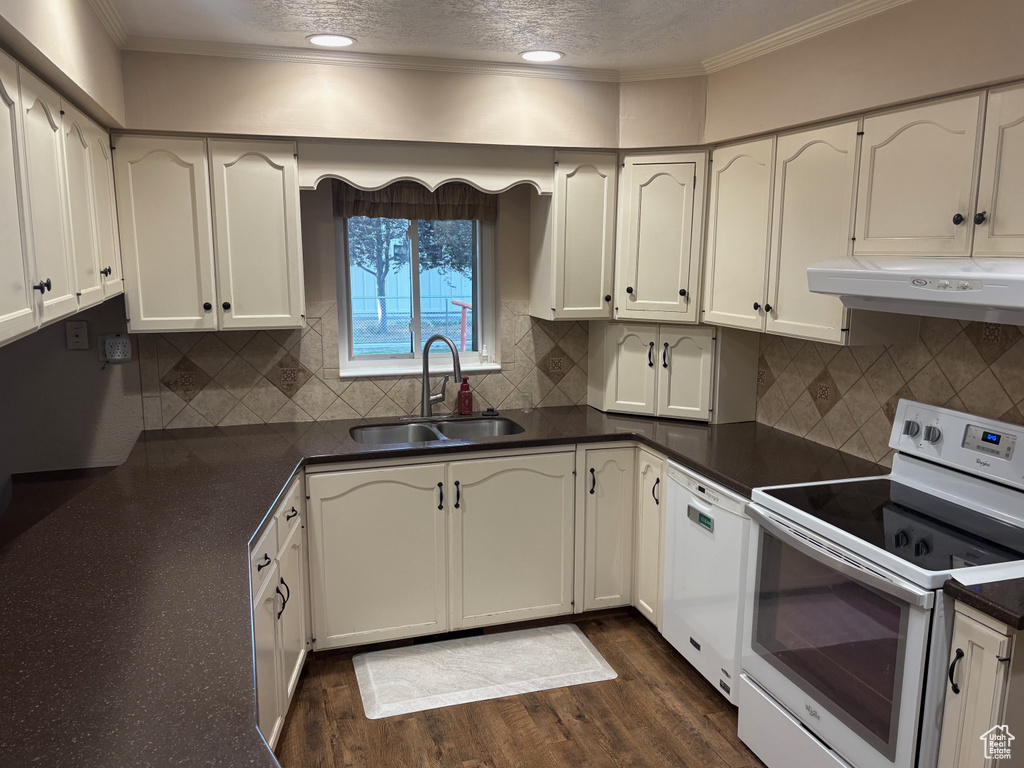 Kitchen featuring white appliances, a sink, dark countertops, under cabinet range hood, and crown molding