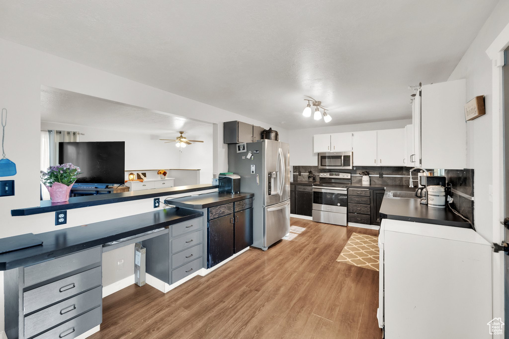 Kitchen featuring stainless steel appliances, dark countertops, a sink, light wood-type flooring, and tasteful backsplash