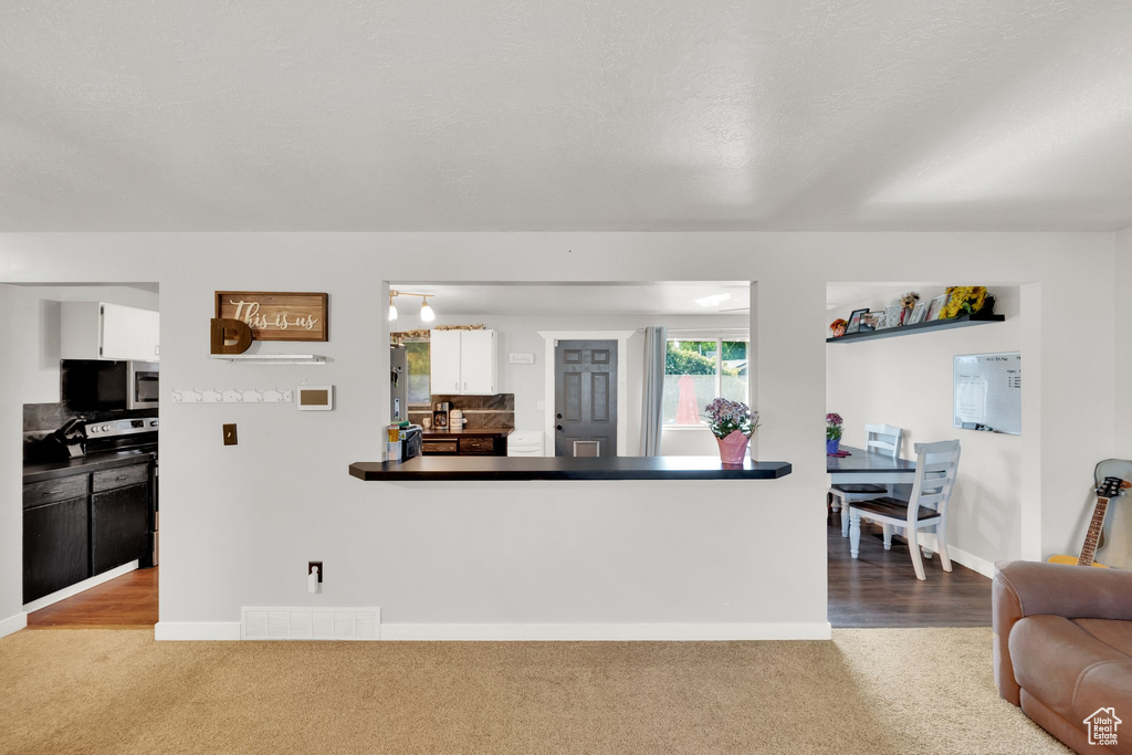 Kitchen featuring stainless steel microwave, electric range oven, carpet flooring, white cabinets, and baseboards