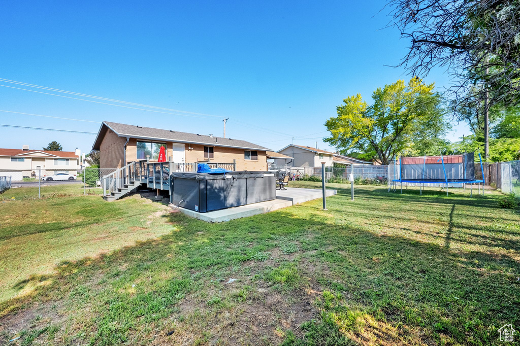 Rear view of house featuring a hot tub, a trampoline, and a deck