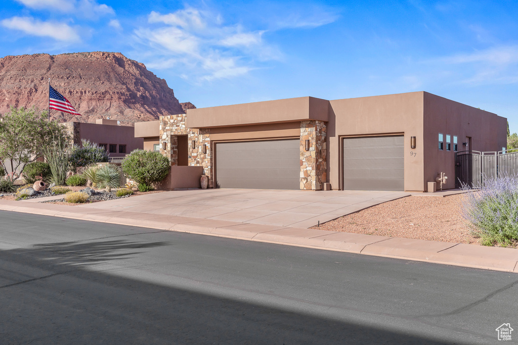 Southwest-style home featuring an attached garage, stucco siding, a mountain view, stone siding, and driveway
