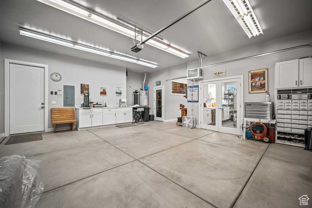 Garage with electric panel, a garage door opener, strapped water heater, and a sink