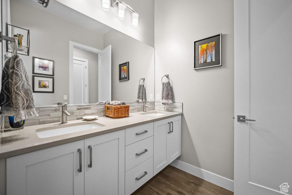 Full bathroom featuring double vanity, backsplash, wood finished floors, and baseboards