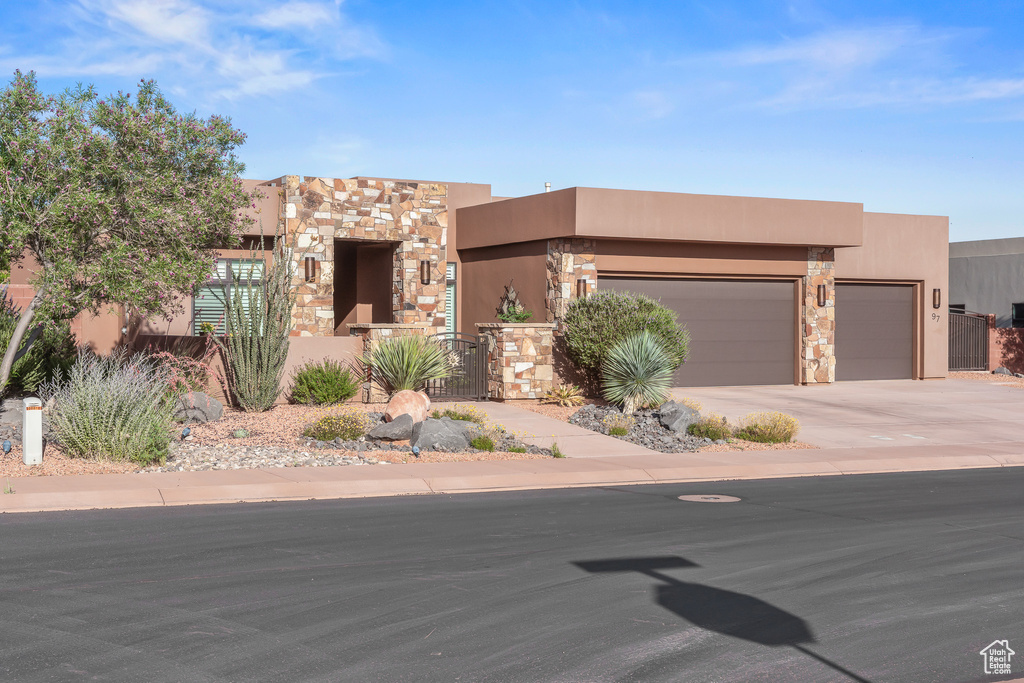 Pueblo-style house with stucco siding, an attached garage, stone siding, and driveway