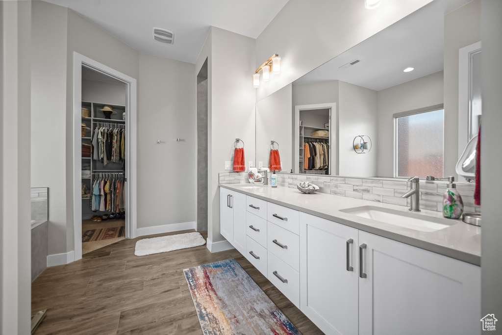 Bathroom featuring double vanity, wood finished floors, a spacious closet, decorative backsplash, and baseboards