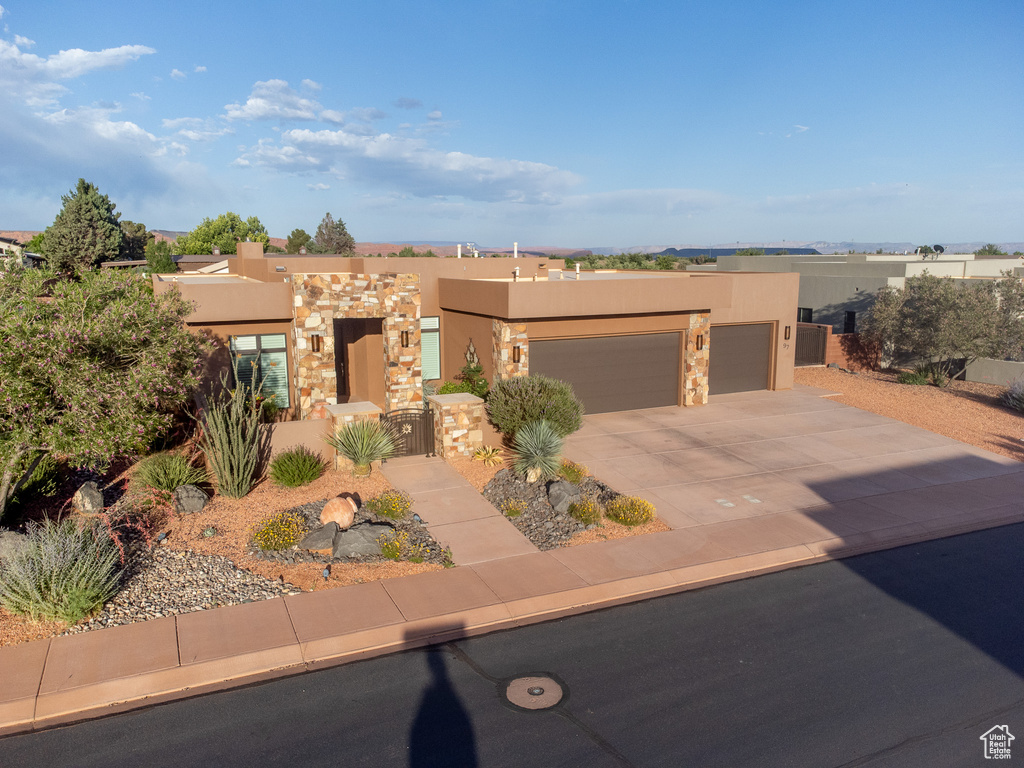 Adobe home featuring stucco siding, an attached garage, driveway, a gate, and stone siding