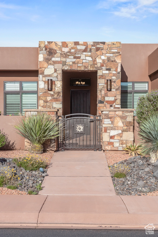 Entrance to property with a gate, stucco siding, and stone siding