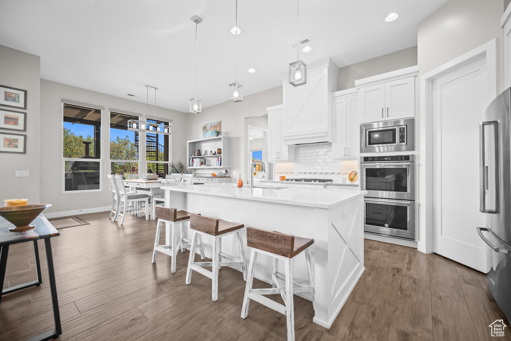 Kitchen featuring appliances with stainless steel finishes, a sink, white cabinets, a breakfast bar, and backsplash