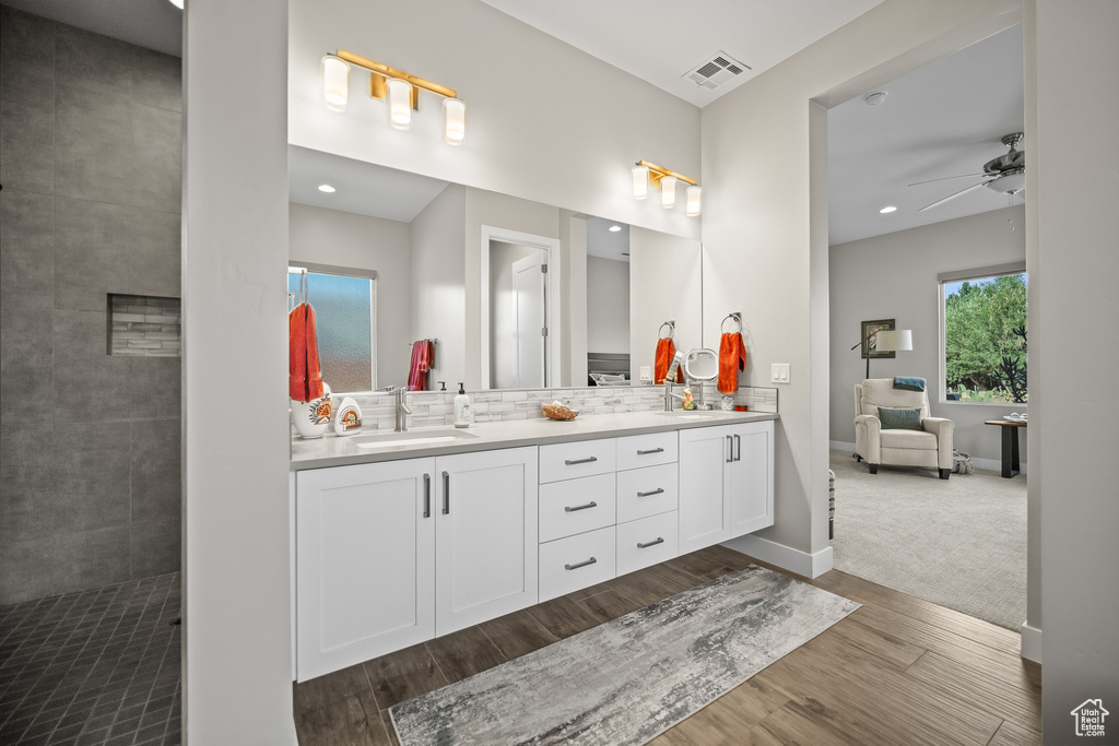 Full bathroom with double vanity, wood finished floors, tasteful backsplash, ceiling fan, and a tile shower
