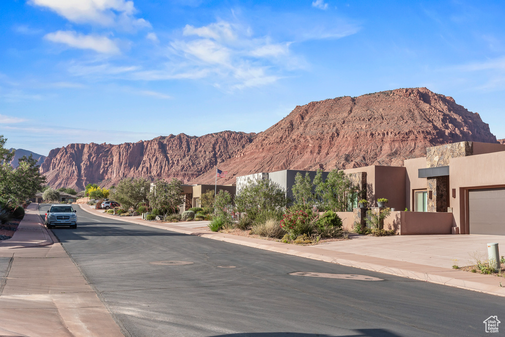 View of asphalt road featuring sidewalks, a mountain view, and curbs