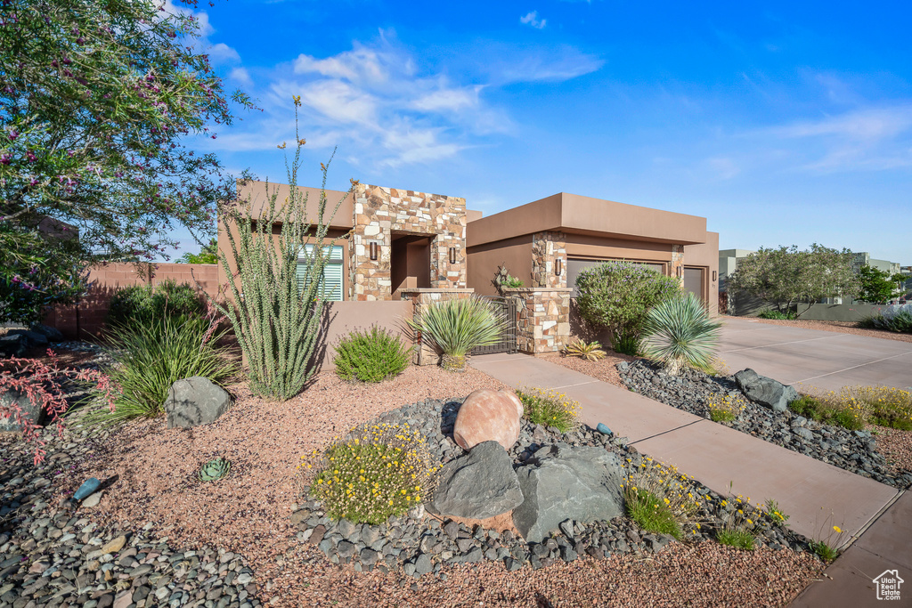 Pueblo-style house with a fenced front yard, driveway, stucco siding, and an attached garage