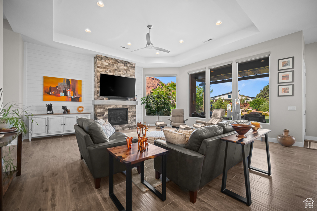 Living area with a tray ceiling, ceiling fan, dark wood-style flooring, recessed lighting, and a fireplace