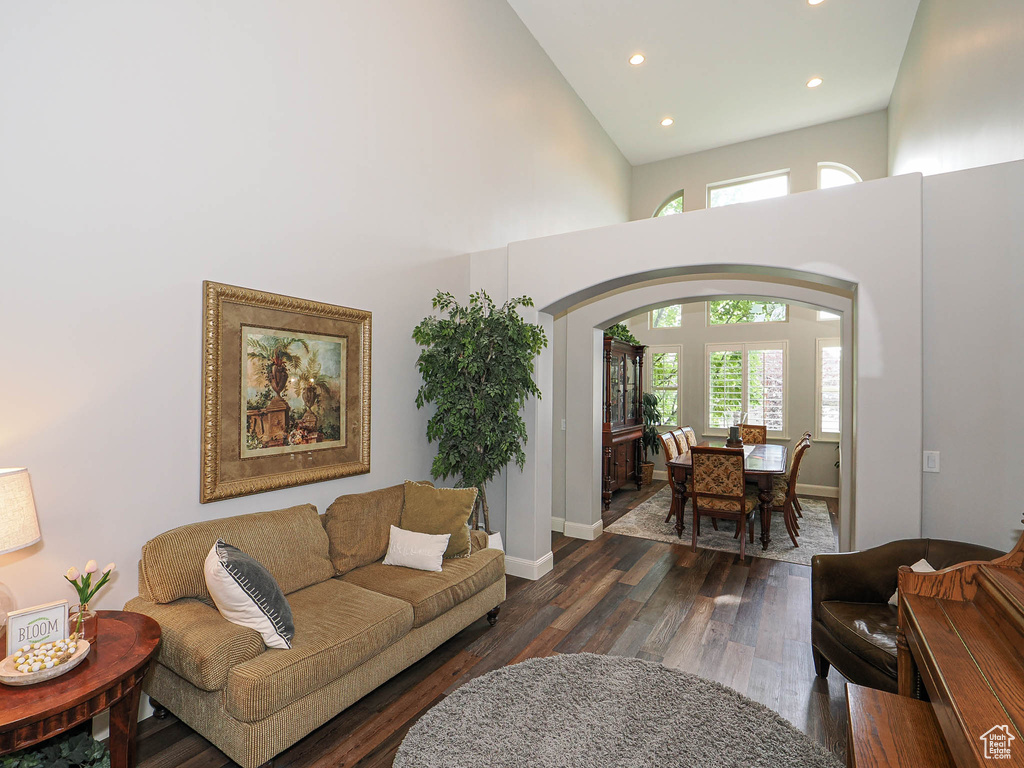 Living area with a towering ceiling, recessed lighting, arched walkways, dark wood finished floors, and baseboards
