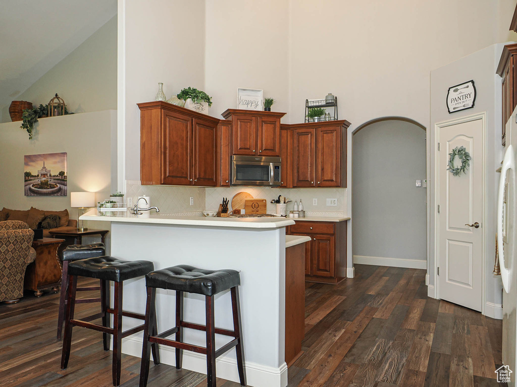 Kitchen with high vaulted ceiling, stainless steel microwave, a breakfast bar area, dark wood-type flooring, and light countertops