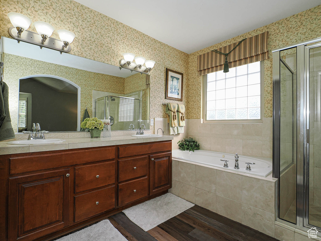 Full bathroom with wood finished floors, a stall shower, a garden tub, double vanity, and wallpapered walls