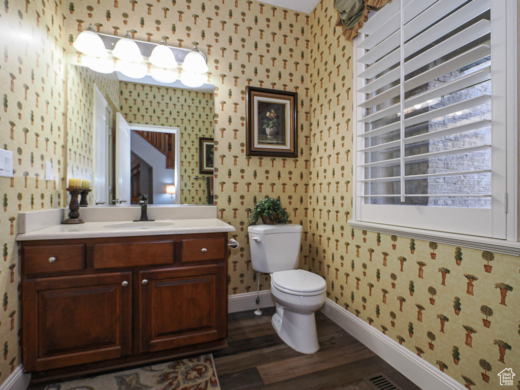 Bathroom featuring wallpapered walls, baseboards, toilet, wood finished floors, and vanity