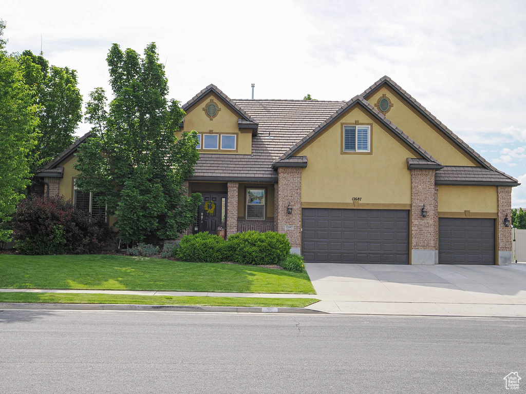 Traditional home featuring stucco siding, a front lawn, driveway, a garage, and a tiled roof