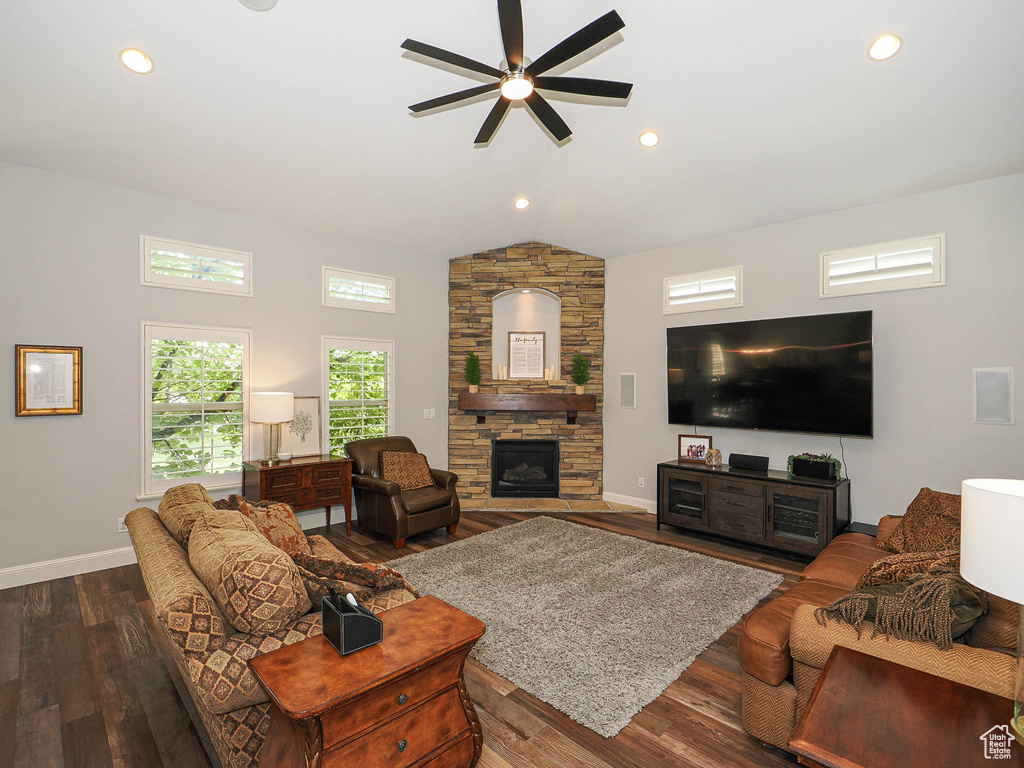 Living room with a ceiling fan, a stone fireplace, lofted ceiling, baseboards, and dark wood-style floors