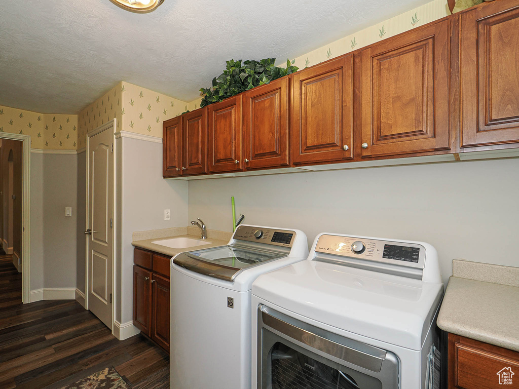 Laundry area with wallpapered walls, separate washer and dryer, cabinet space, dark wood-style floors, and baseboards