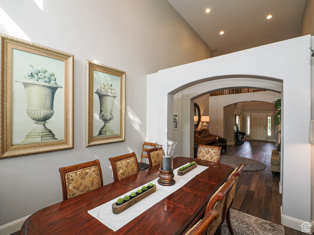 Dining space with arched walkways, recessed lighting, wood finished floors, high vaulted ceiling, and baseboards
