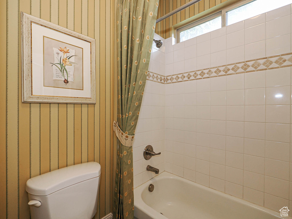 Full bath featuring wallpapered walls, shower / tub combo, and toilet
