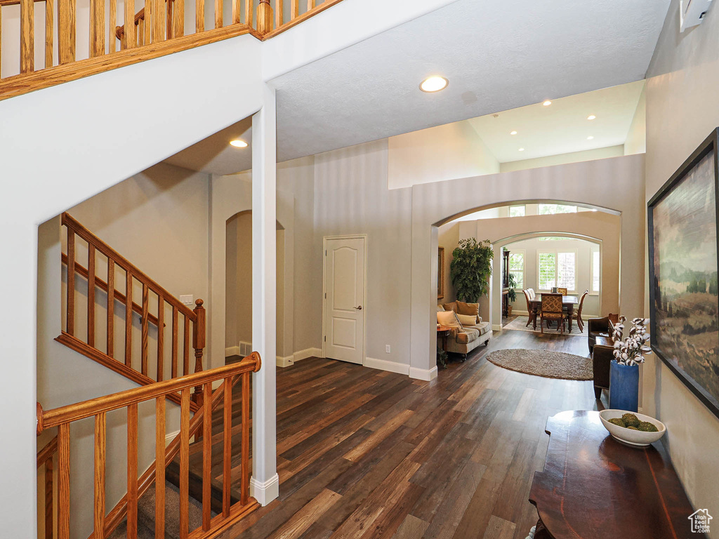 Foyer with arched walkways, wood finished floors, a high ceiling, stairs, and baseboards