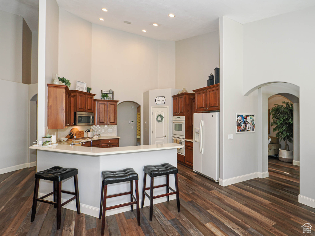 Kitchen with white appliances, a high ceiling, arched walkways, a peninsula, and baseboards