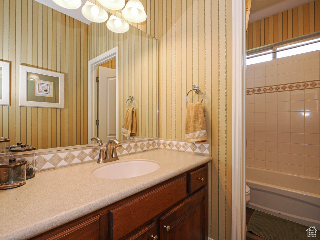 Full bathroom featuring vanity, wallpapered walls, toilet, a chandelier, and  shower combination