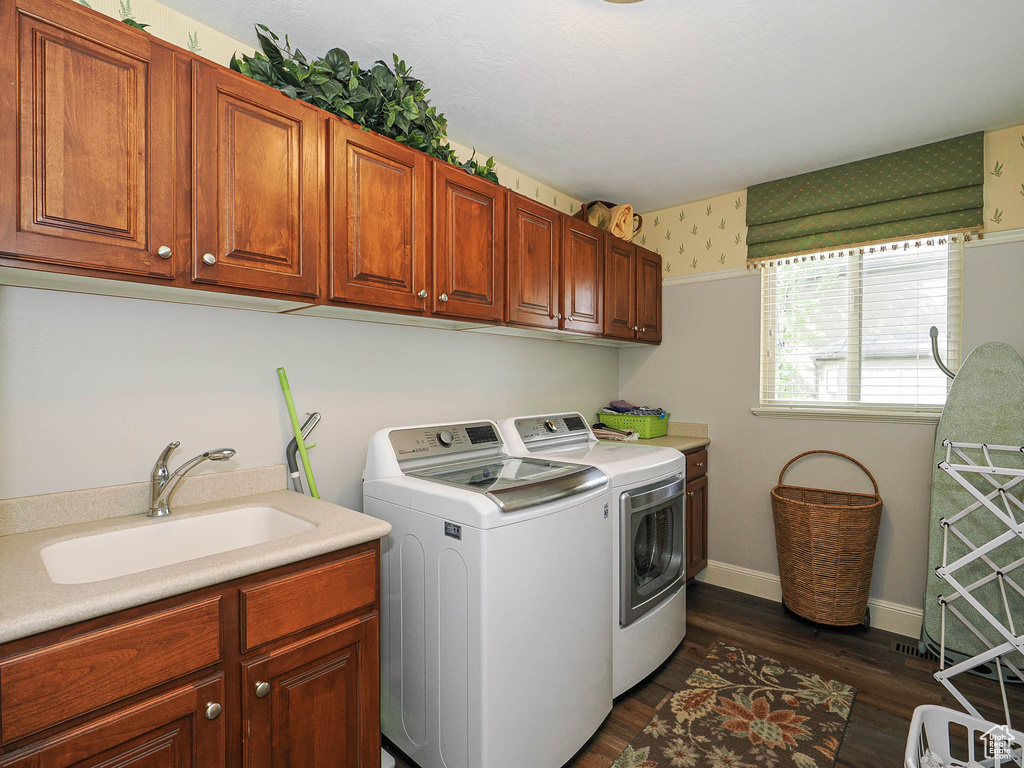 Washroom with separate washer and dryer, cabinet space, wallpapered walls, dark wood-style flooring, and baseboards