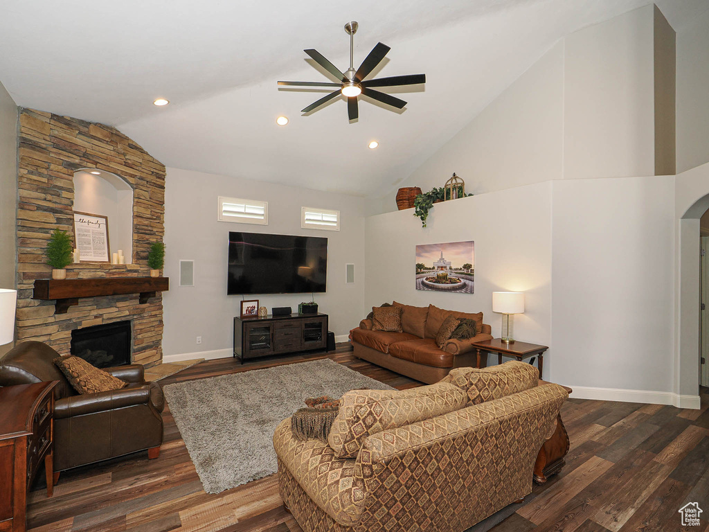 Living area with a ceiling fan, dark wood-type flooring, a fireplace, arched walkways, and baseboards