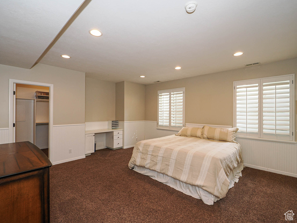 Bedroom featuring a wainscoted wall, dark colored carpet, recessed lighting, an office area, and a spacious closet