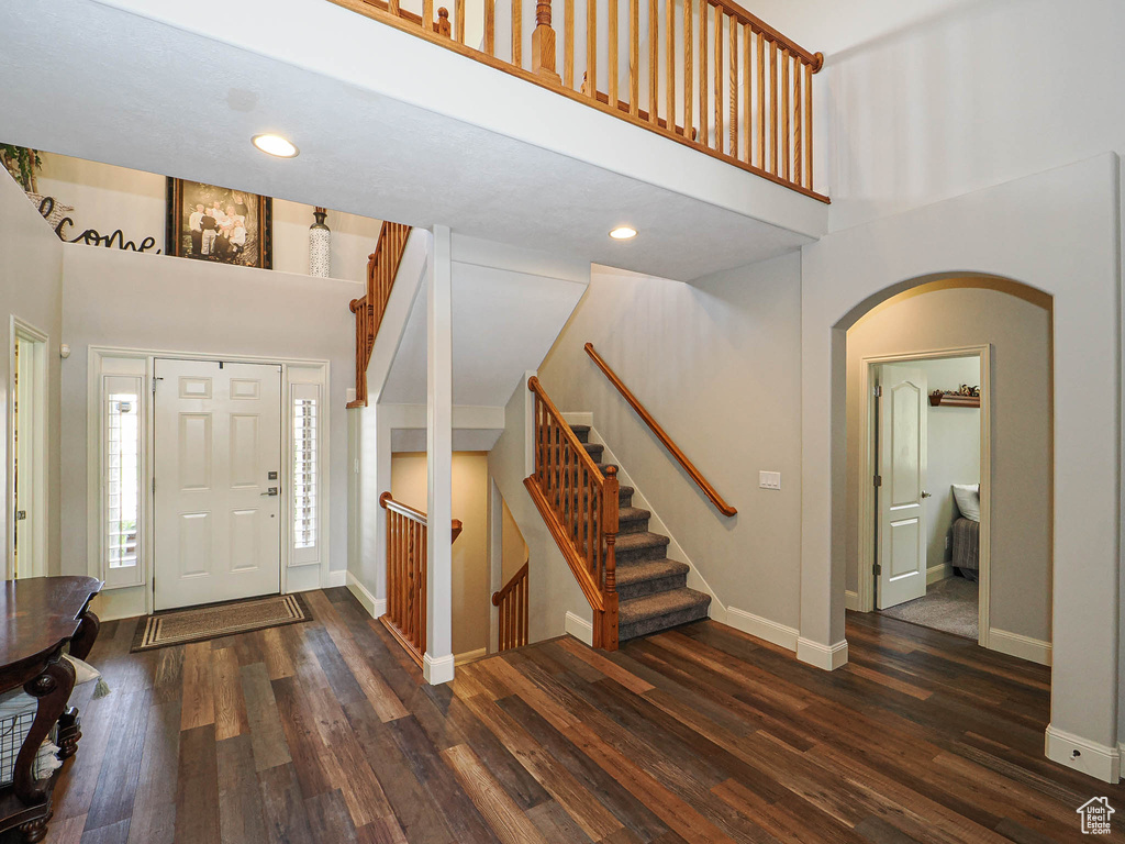 Entrance foyer featuring a towering ceiling, arched walkways, wood finished floors, baseboards, and stairway
