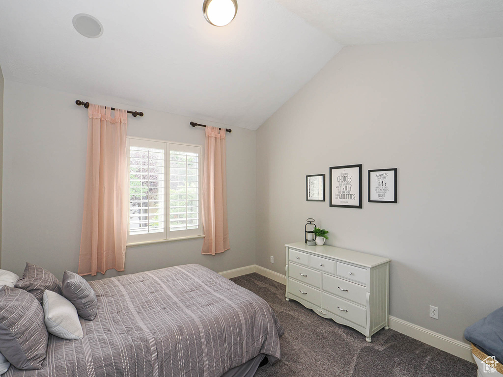 Bedroom with dark colored carpet, lofted ceiling, and baseboards