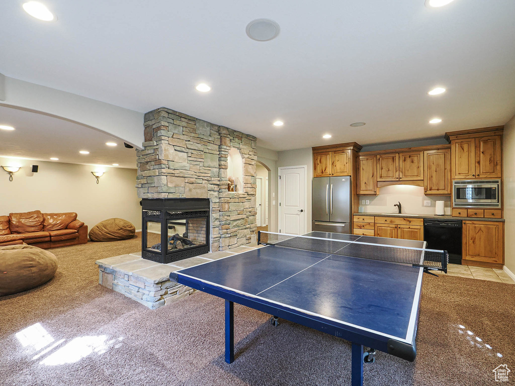 Recreation room featuring arched walkways, a sink, light colored carpet, recessed lighting, and a fireplace