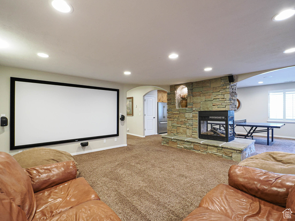 Carpeted home theater featuring arched walkways, baseboards, recessed lighting, and a stone fireplace