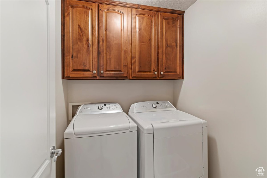Washroom with cabinet space, independent washer and dryer, and a textured ceiling